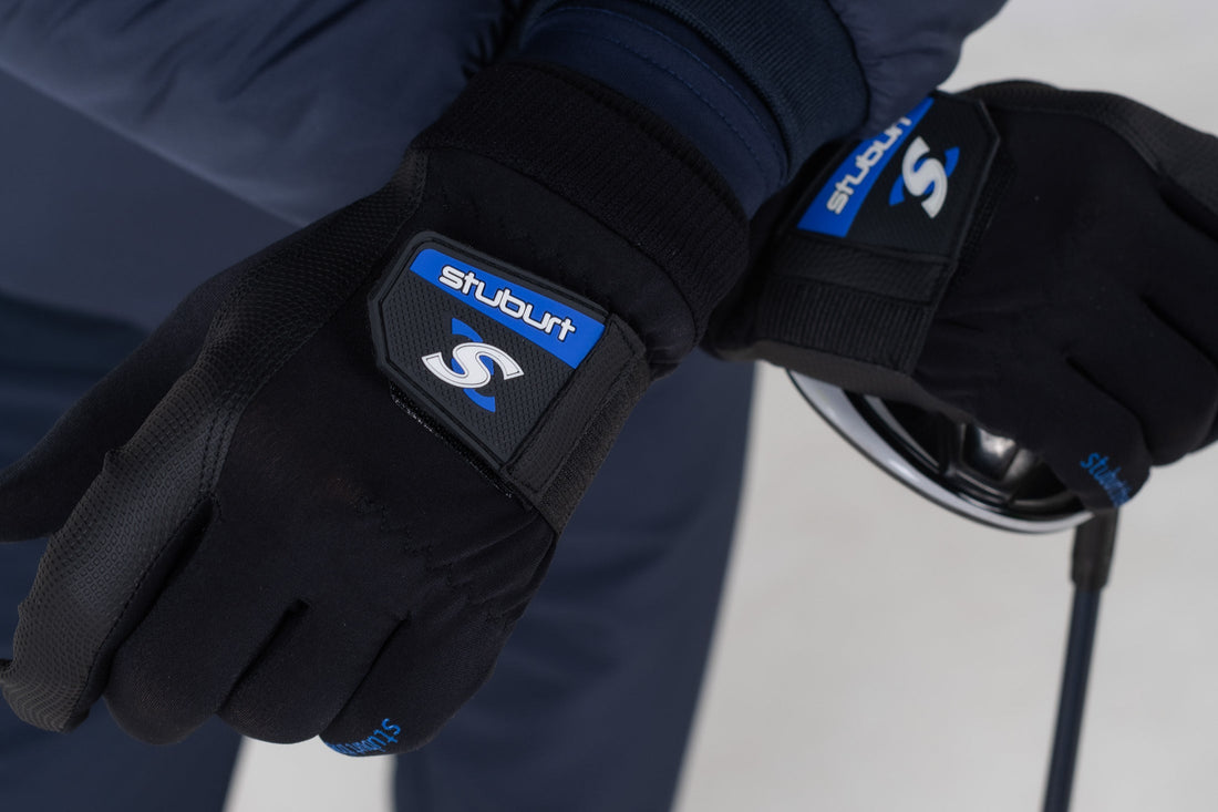 A pair of black Stuburt golf gloves worn on both hands, gripping a driver