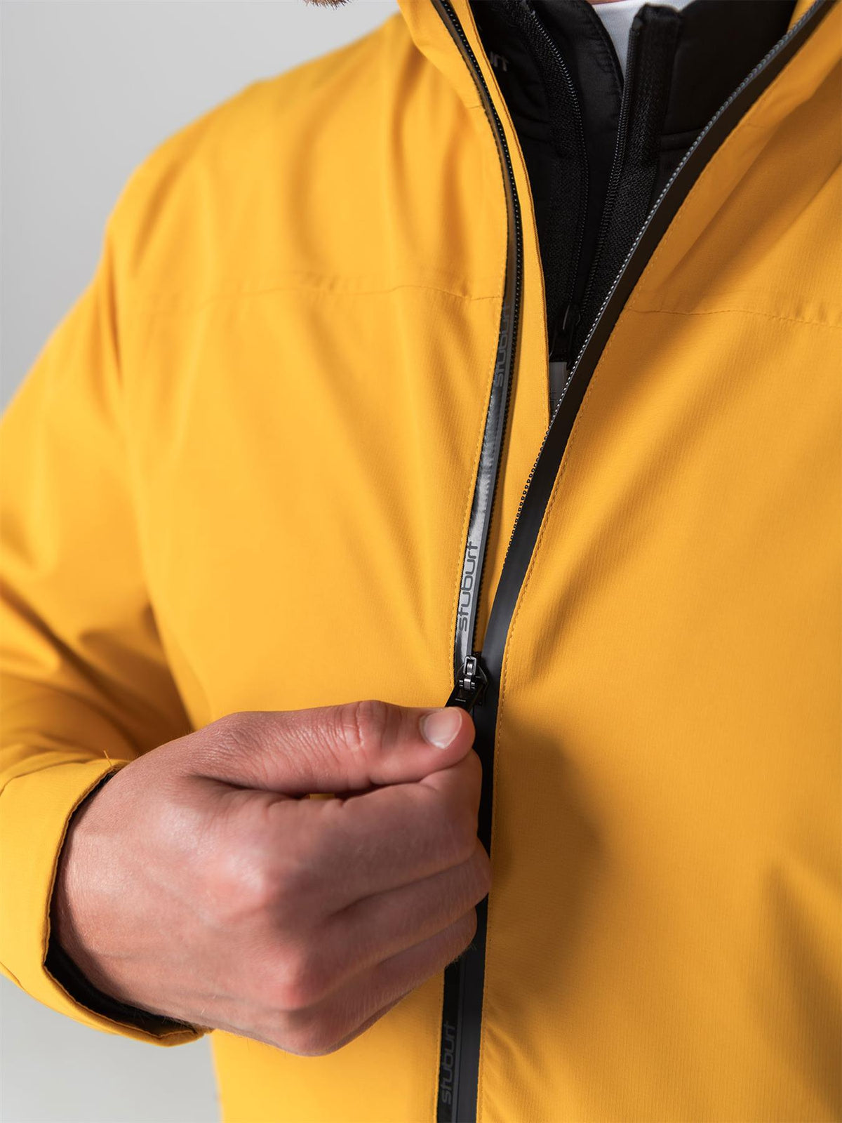 Close-up of the taped seam and water-repellent zip on a yellow Stuburt DRI-back waterproof jacket, pulled up by hand.