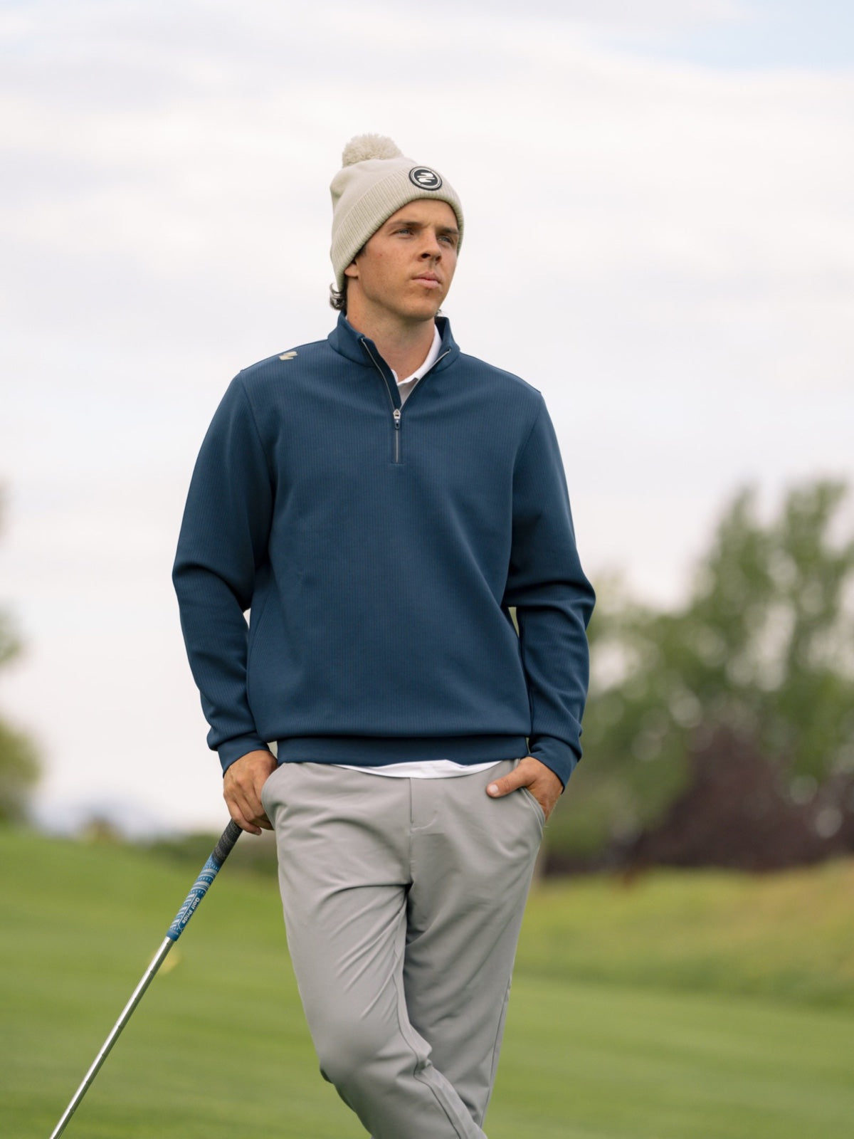Golfer in a navy Stuburt quarter-zip mid-layer and stone bobble hat on the fairway