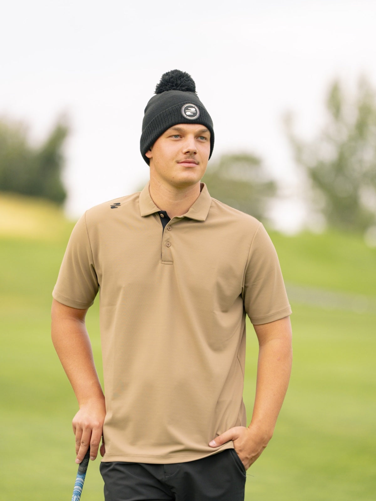 Golfer in a sand Stuburt polo and black bobble hat walking the fairway